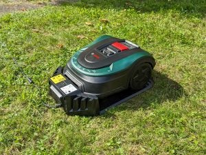 Bosch Home and Garden Indego XS 300 Mähroboter auf der Wiese und in der Ladestation